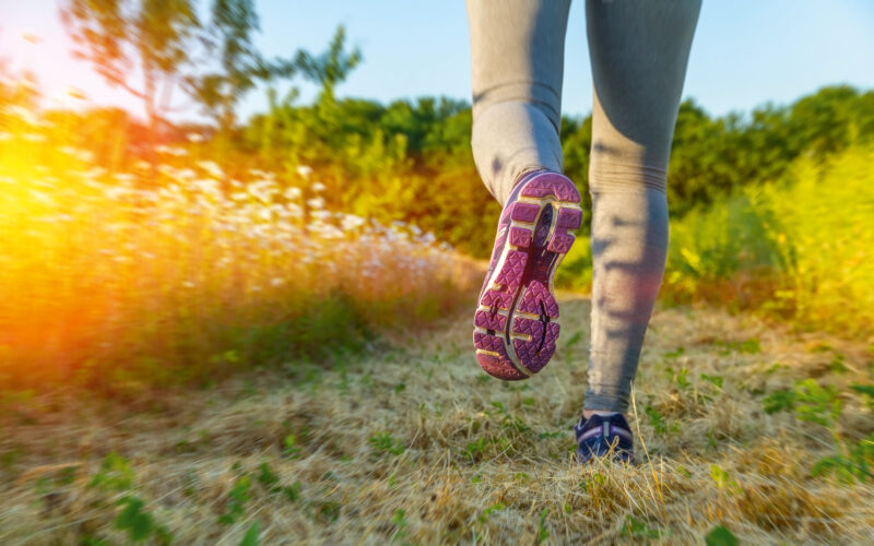 Fitness Girl running at sunset in a path surrounded by fields with colorful outfit